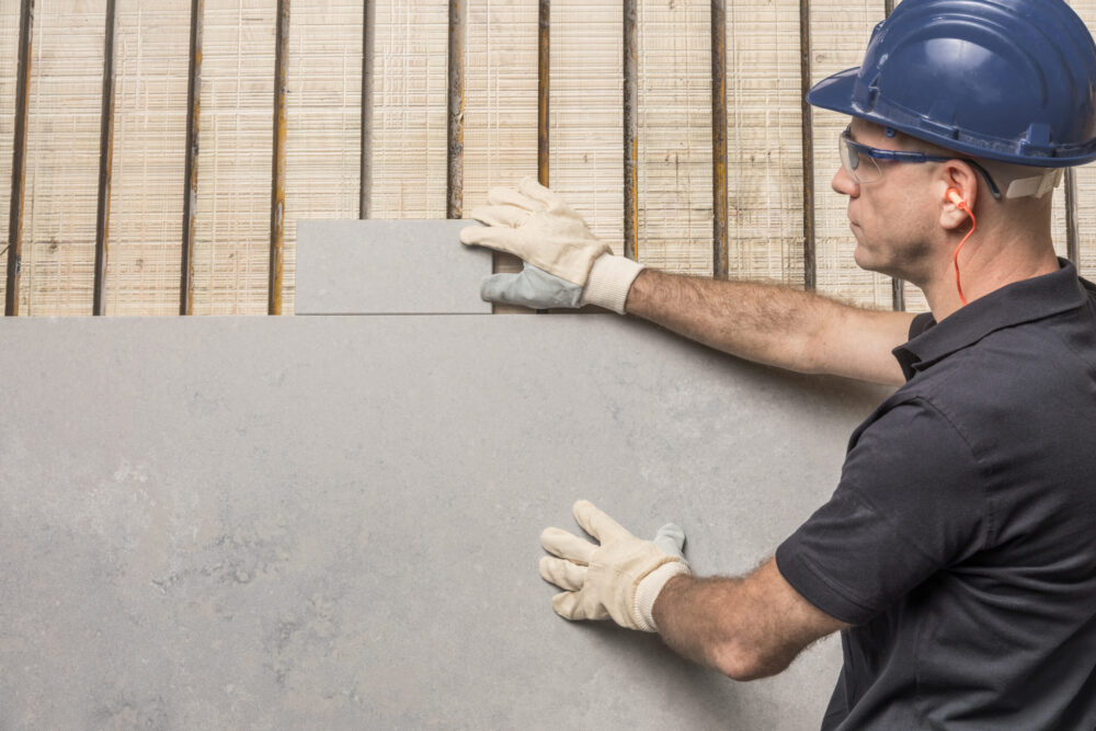 Worker wearing safety gear installing a large gray stone slab.