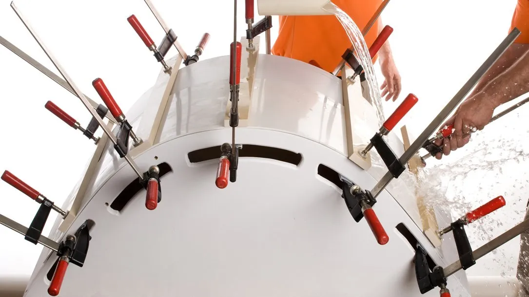 Fabricators shaping a curved Caesarstone quartz surface using clamps and water during the thermoforming process.