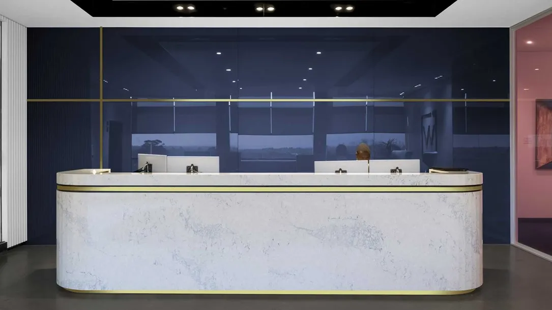 Curved Caesarstone thermoformed reception desk with white quartz surface and brass detailing in a modern office interior.