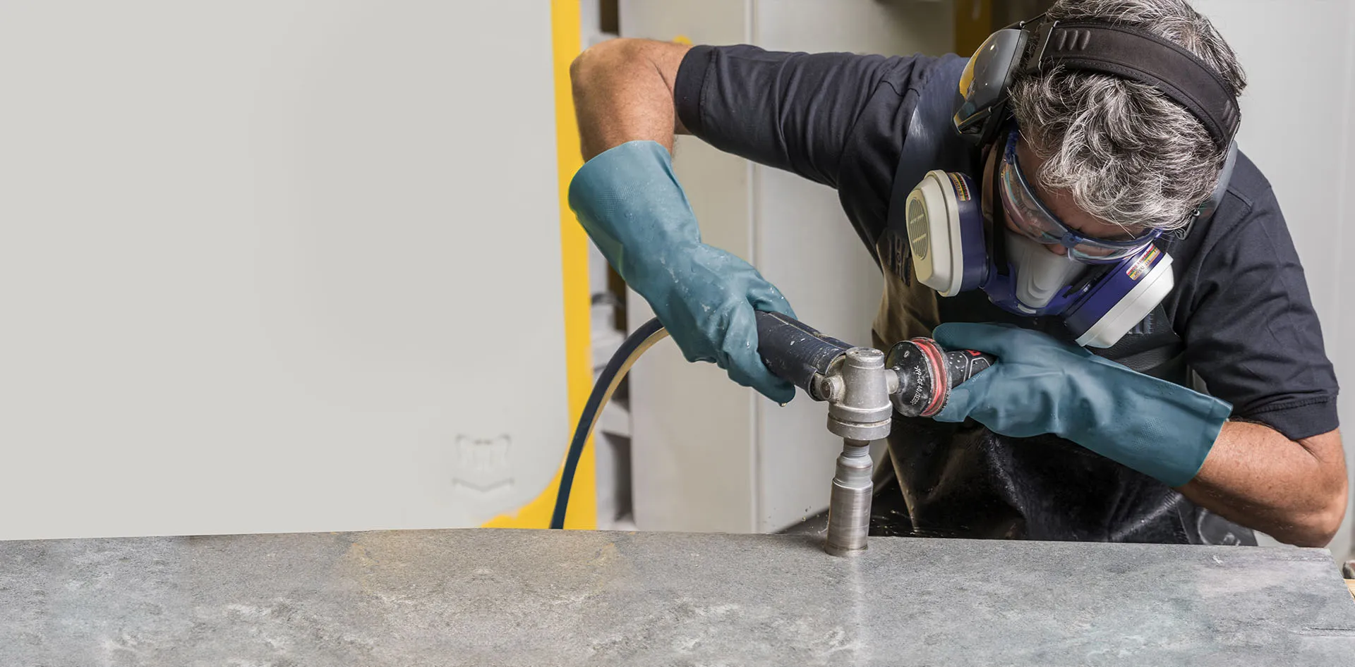 Fabricator polishing a Caesarstone surface using a power tool, wearing protective gloves, mask, and ear protection.