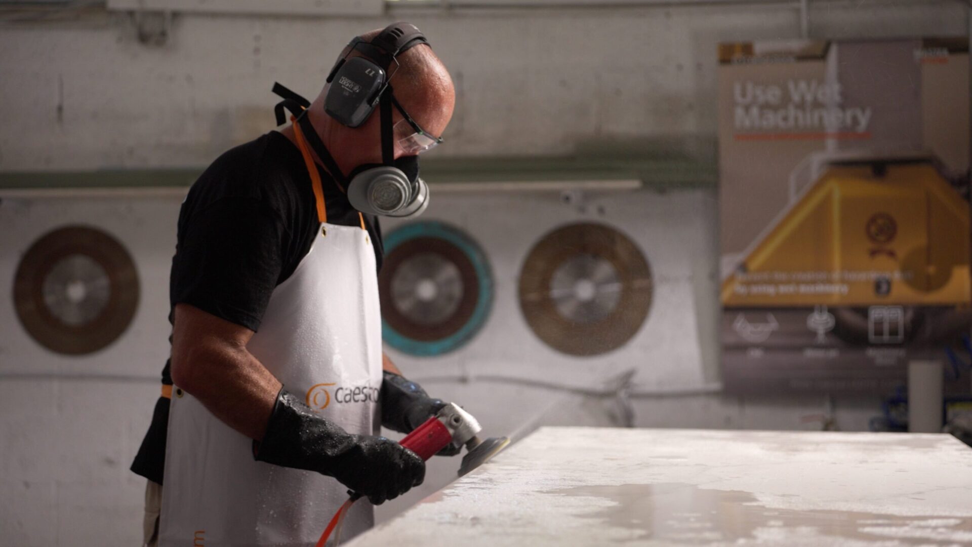 A worker wearing protective gear polishes or grinds a Caesarstone Porcelain surface in an industrial setting.
